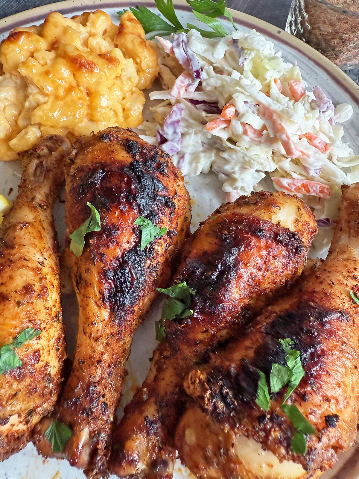 A plate of oven-baked chicken drumsticks served with mac and cheese and coleslaw.