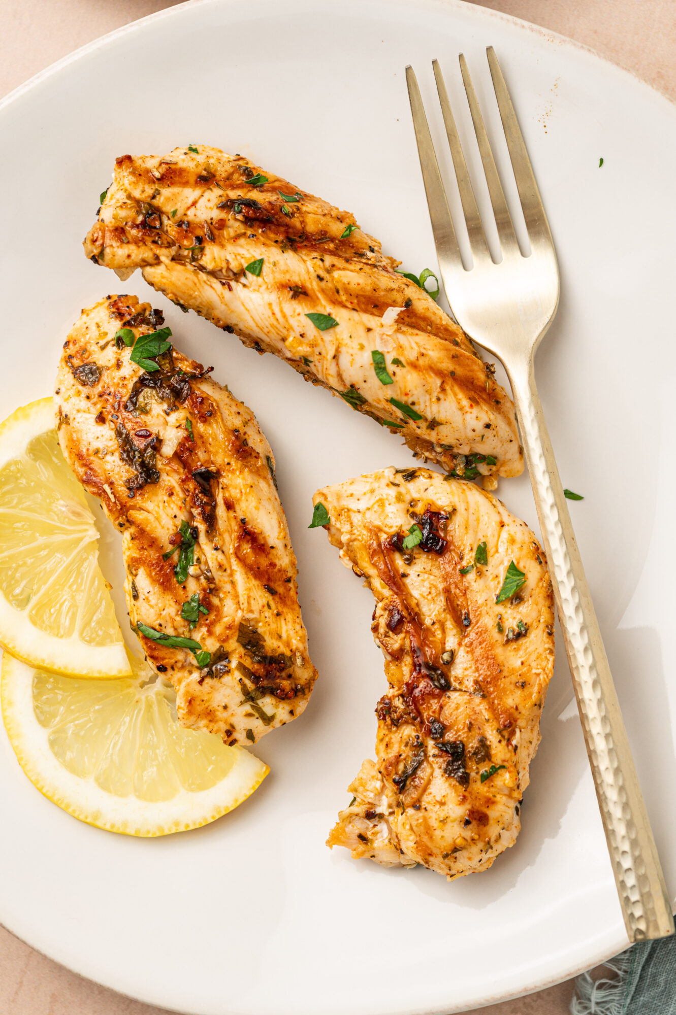 A serving of grilled chicken tenders on a white plate with a fork.