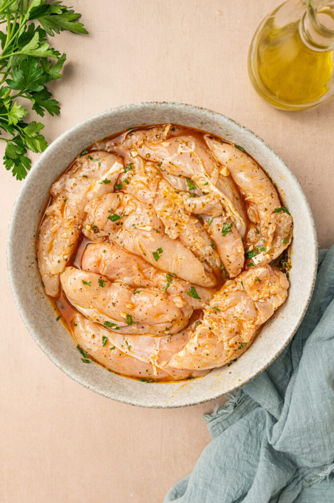 Raw chicken tenders marinating in a bowl.