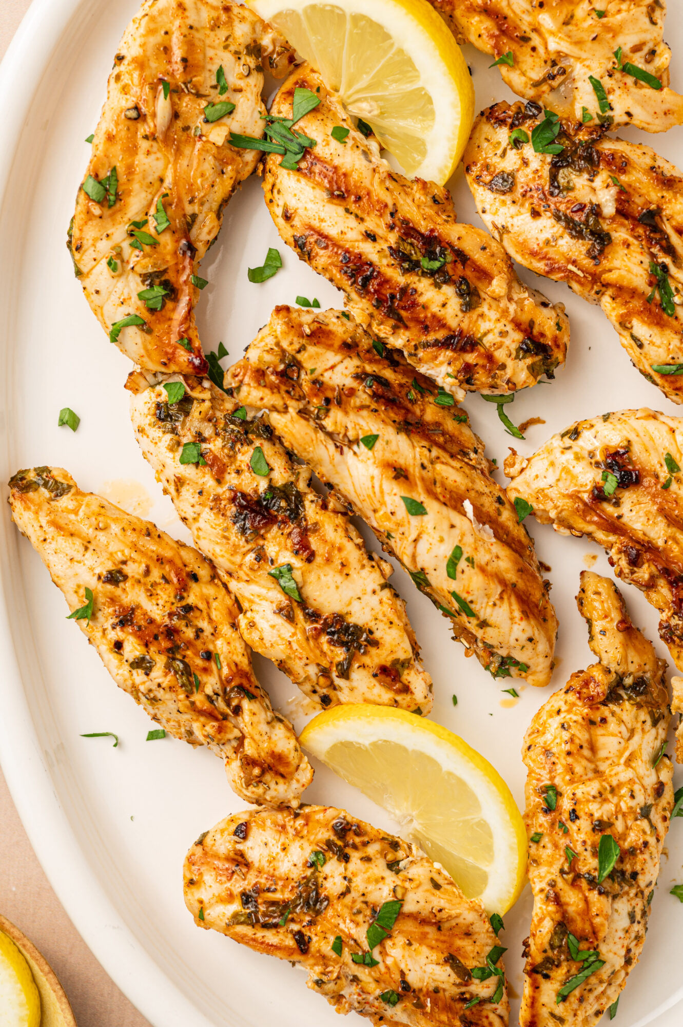 Close-up of grilled chicken tenders on a white serving plate.