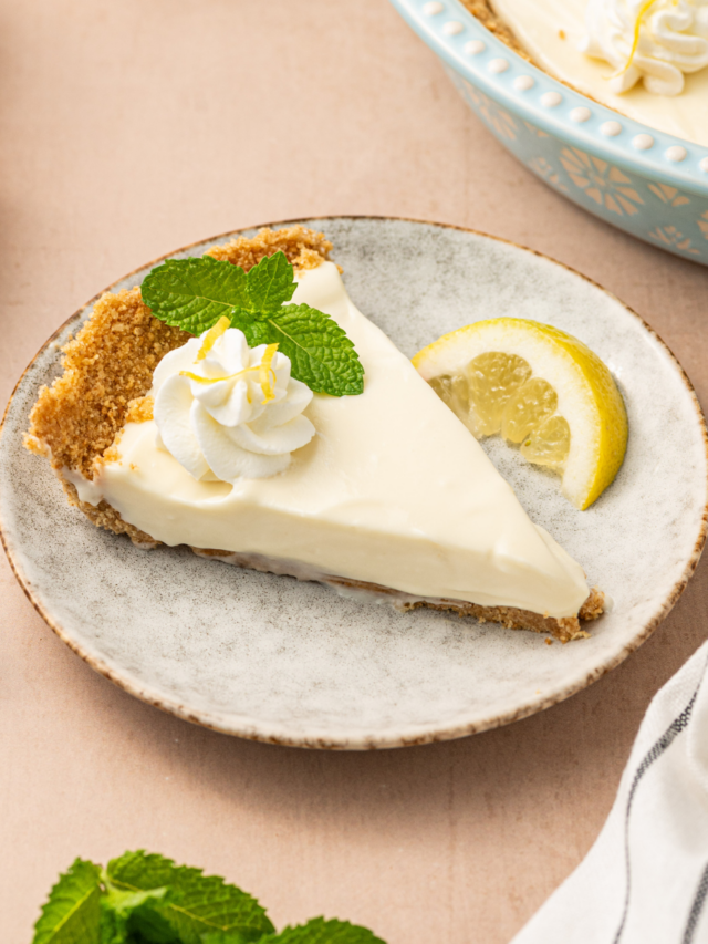 A slice of no-bake lemon icebox pie on a white plate garnished with mint and served with a lemon wedge.