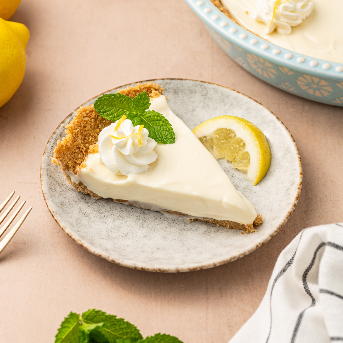 A slice of no-bake lemon icebox pie on a white plate garnished with mint and served with a lemon wedge.