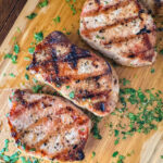 Lemon Dijon grilled pork chops on a wooden cutting board with herbs.