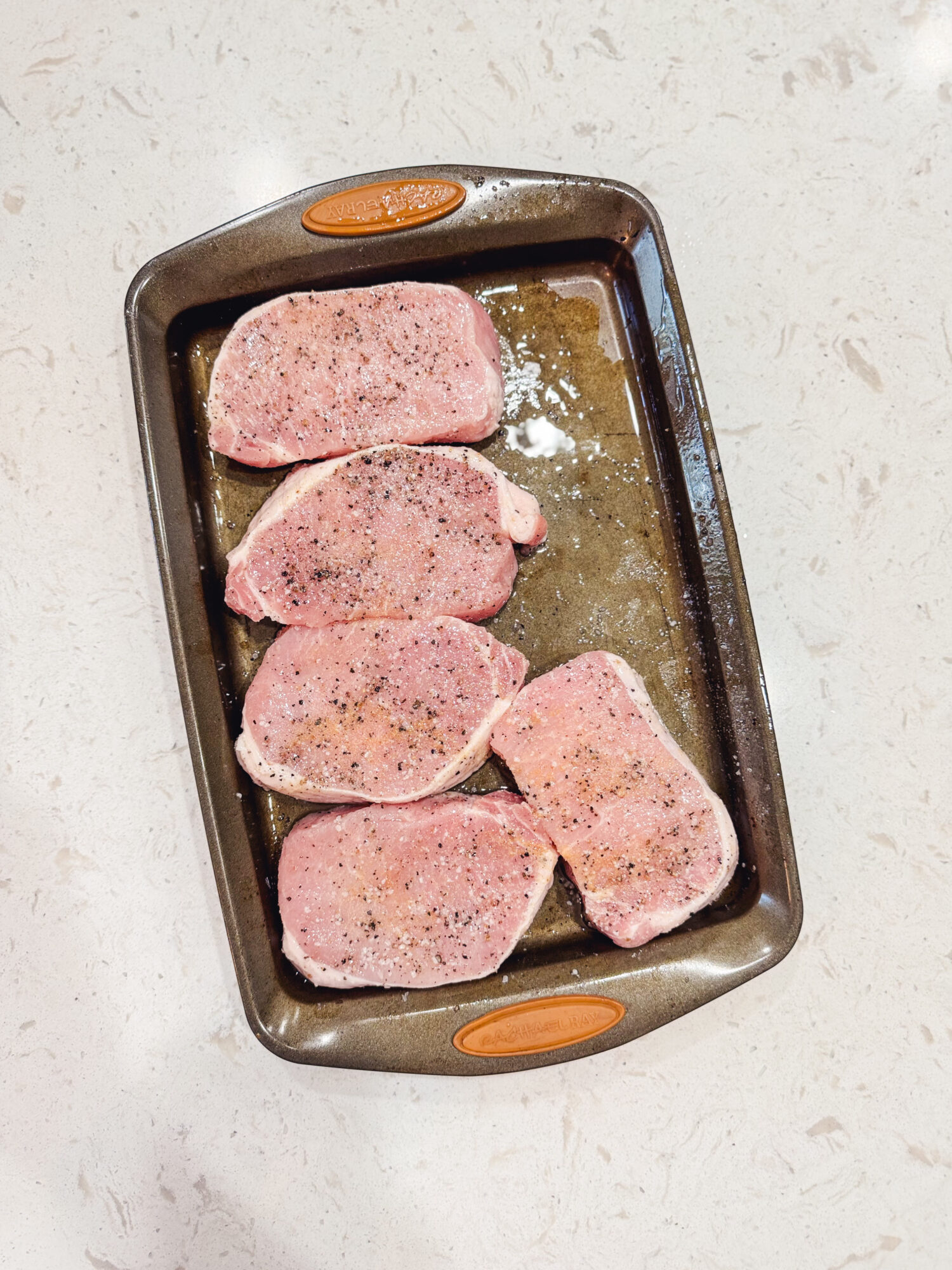 Pork chops on a baking dish ready to be grilled.