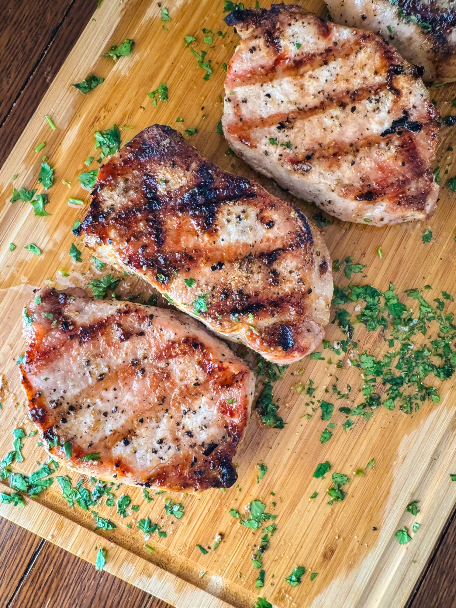 Lemon Dijon grilled pork chops on a wooden cutting board with herbs.