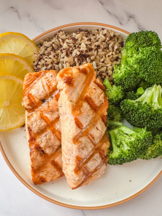 Grilled salmon with lemon butter sauce served with broccoli, lemon slices, and wild rice.