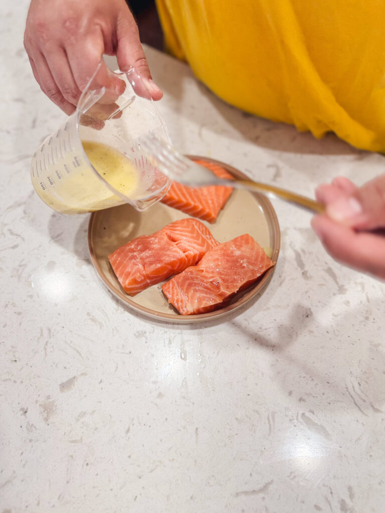 Adding lemon butter sauce to salmon patties on a plate.