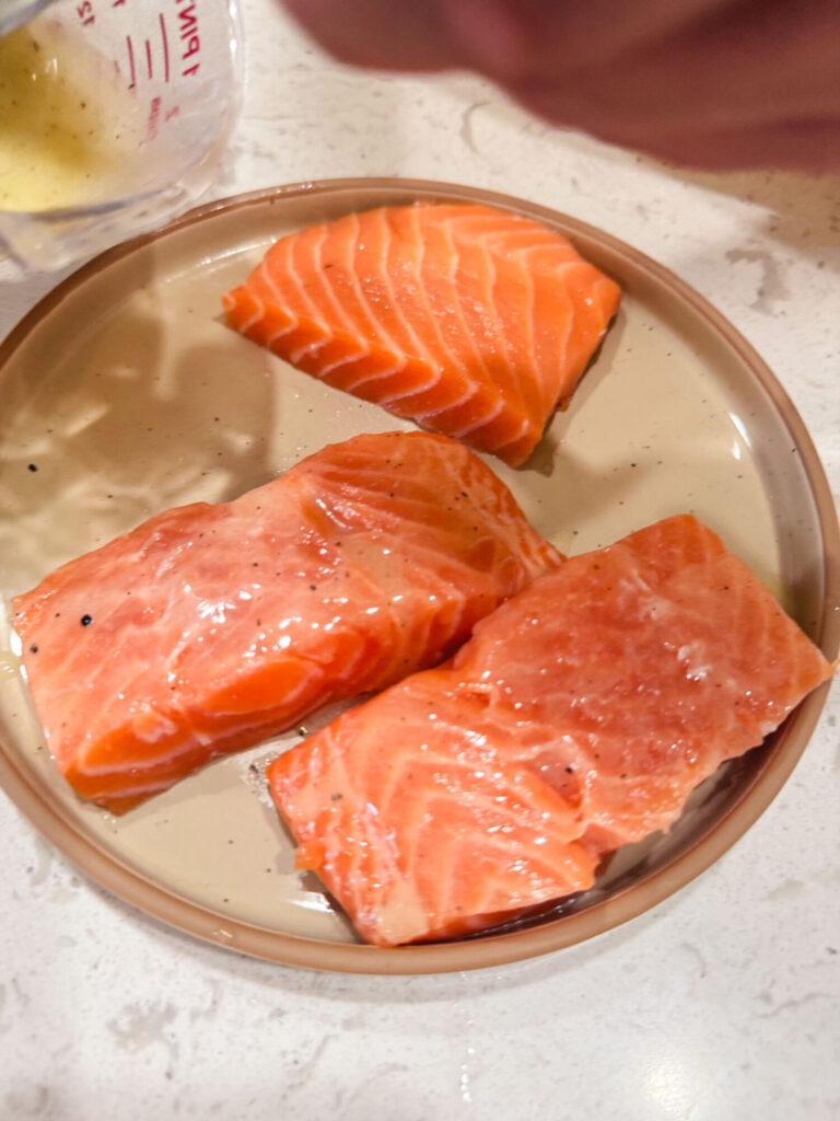 Close-up of adding lemon butter sauce to salmon patties on a plate.