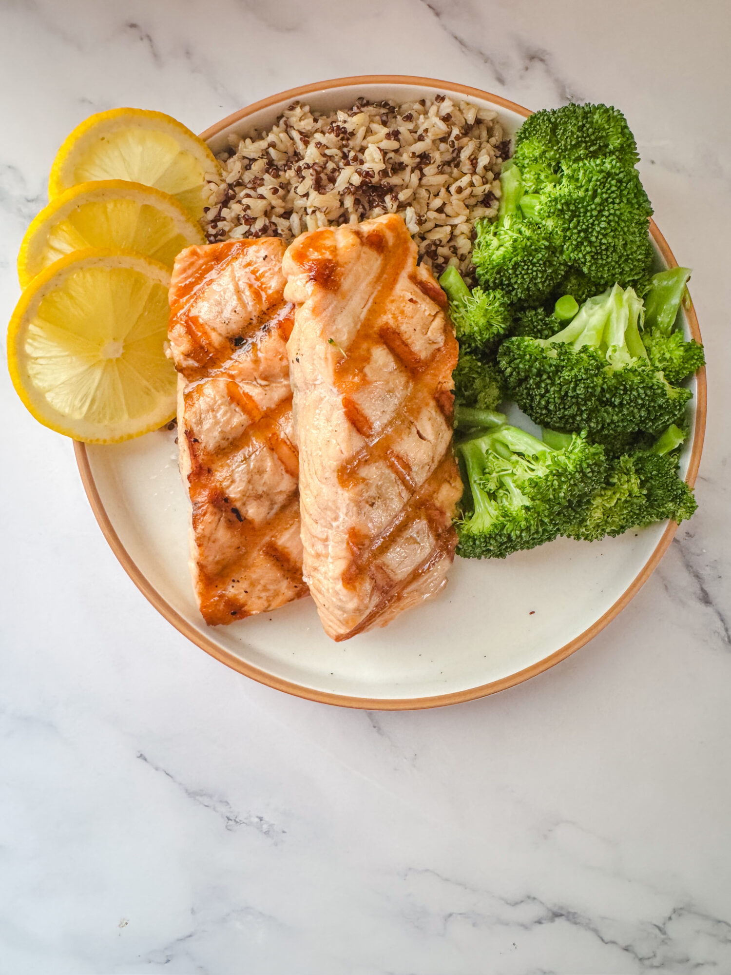 Grilled salmon with lemon butter sauce served with broccoli, lemon slices, and wild rice.