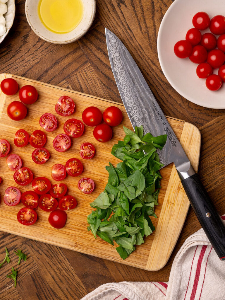 Chopped basil and cherry tomatoes on a cutting board.