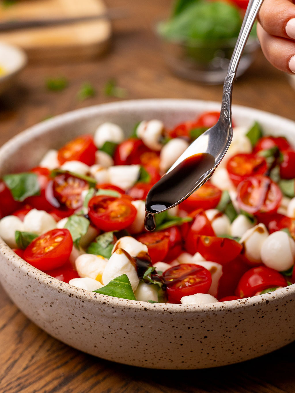Drizzling balsamic glaze onto a caprese salad with a spoon.