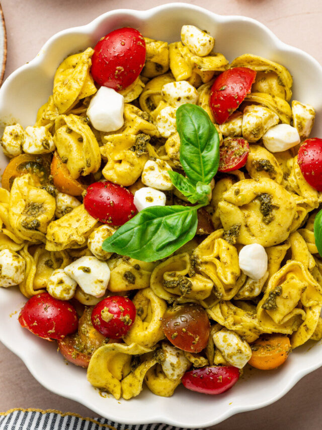 Pesto Tortellini Salad in a serving bowl garnished with basil.