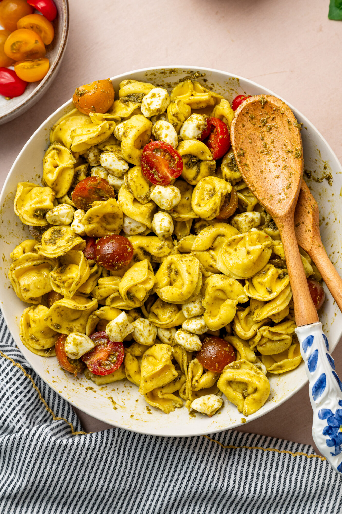 Tossed pesto tortellini salad with two wooden spoons resting on the side.