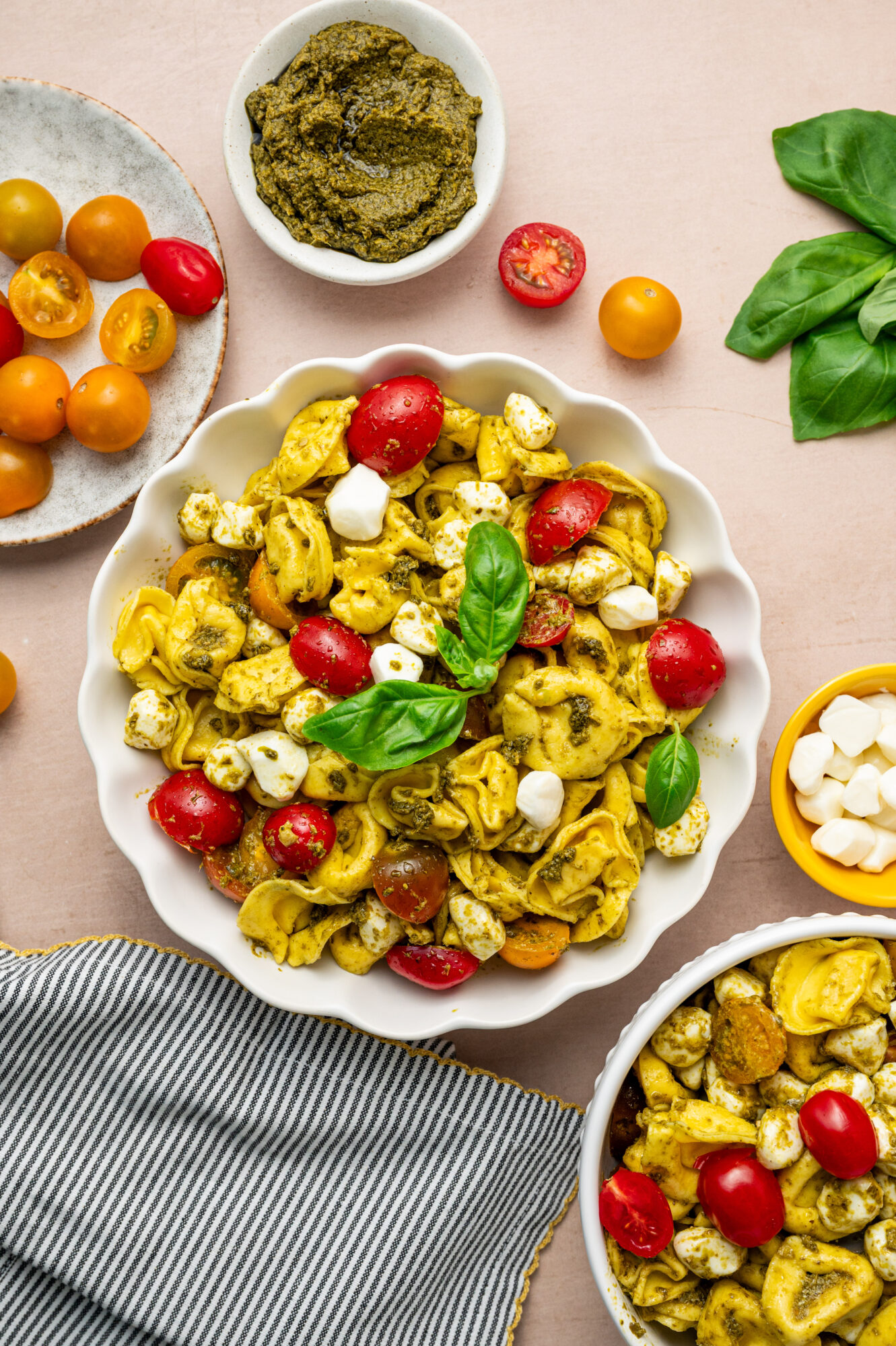 A white bowl of pesto tortellini salad with tomato, mozzarella, and basil.
