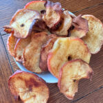 Air fryer apple chips in a bowl on a wooden table.