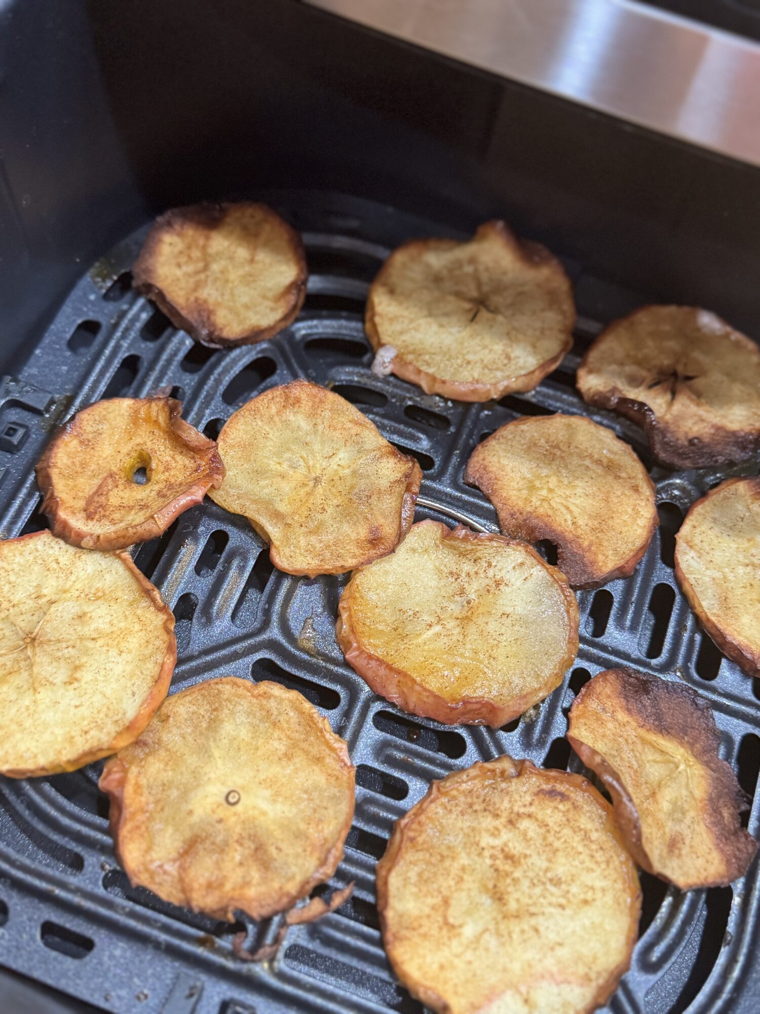 Close-up of golden brown apple chips in an air fryer basket ready to eat.