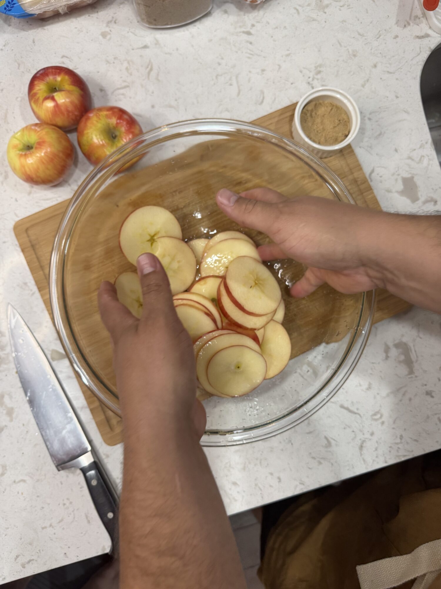 Tossing apple rounds with spices in a glass bowl.