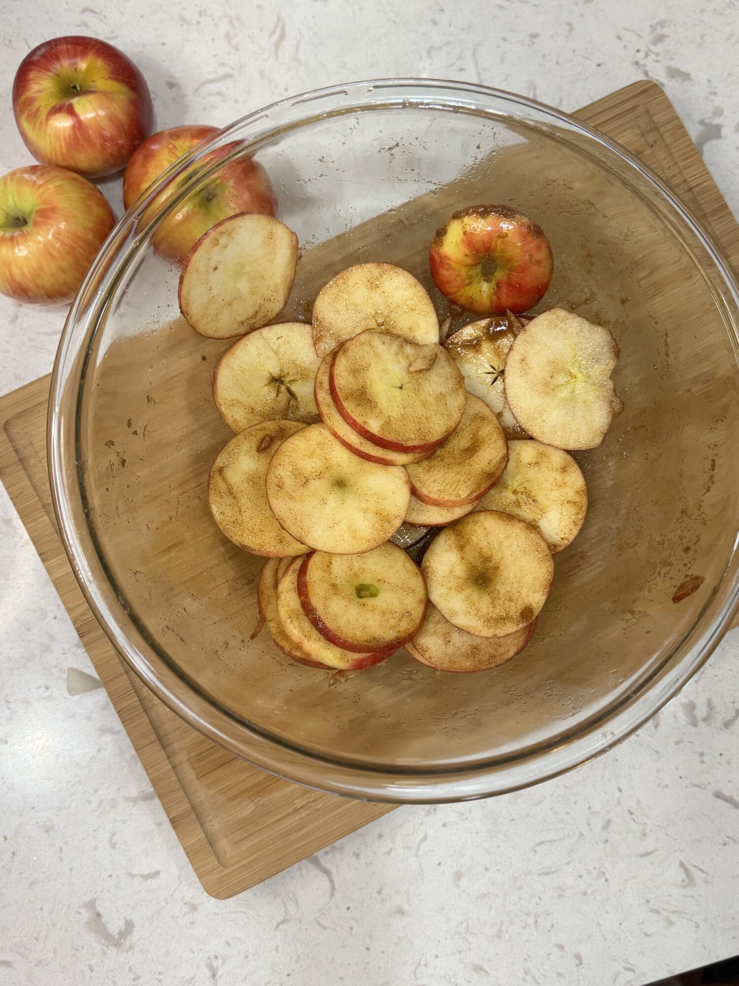 Apple rounds in a glass bowl coated in cinnamon sugar and seasoning.