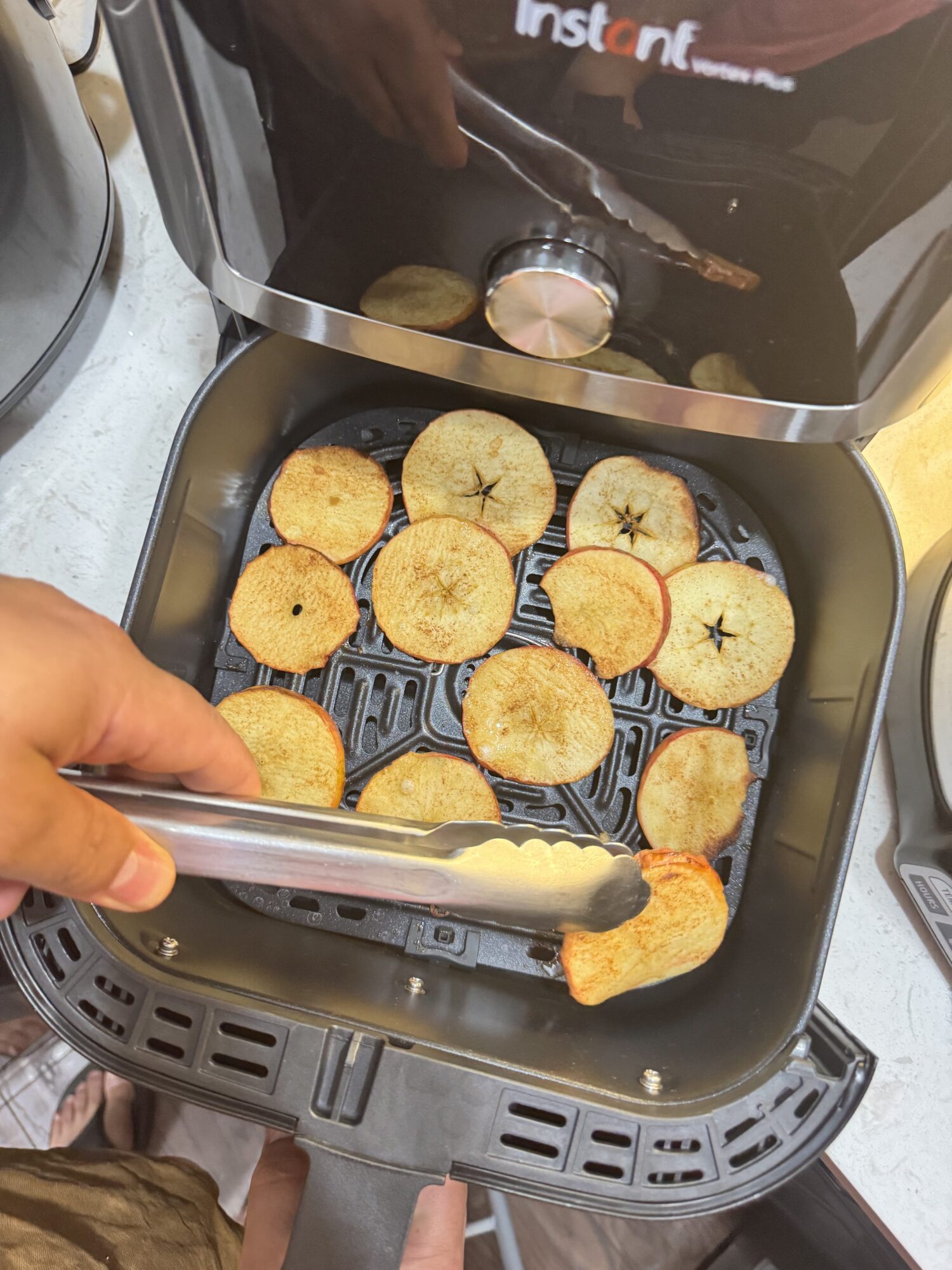 Flipping apple chips in an air fryer basket with a spatula.