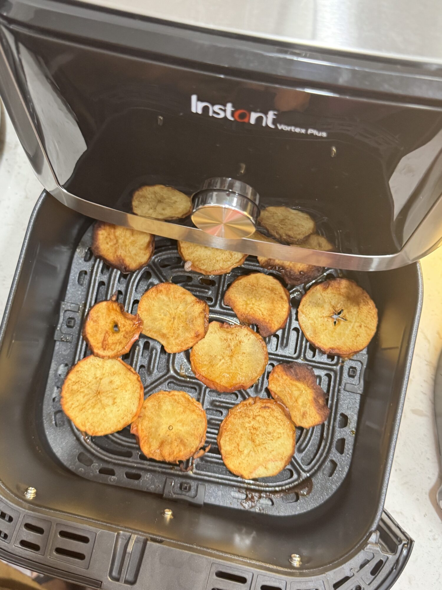 Golden brown apple chips in an air fryer basket ready to eat.