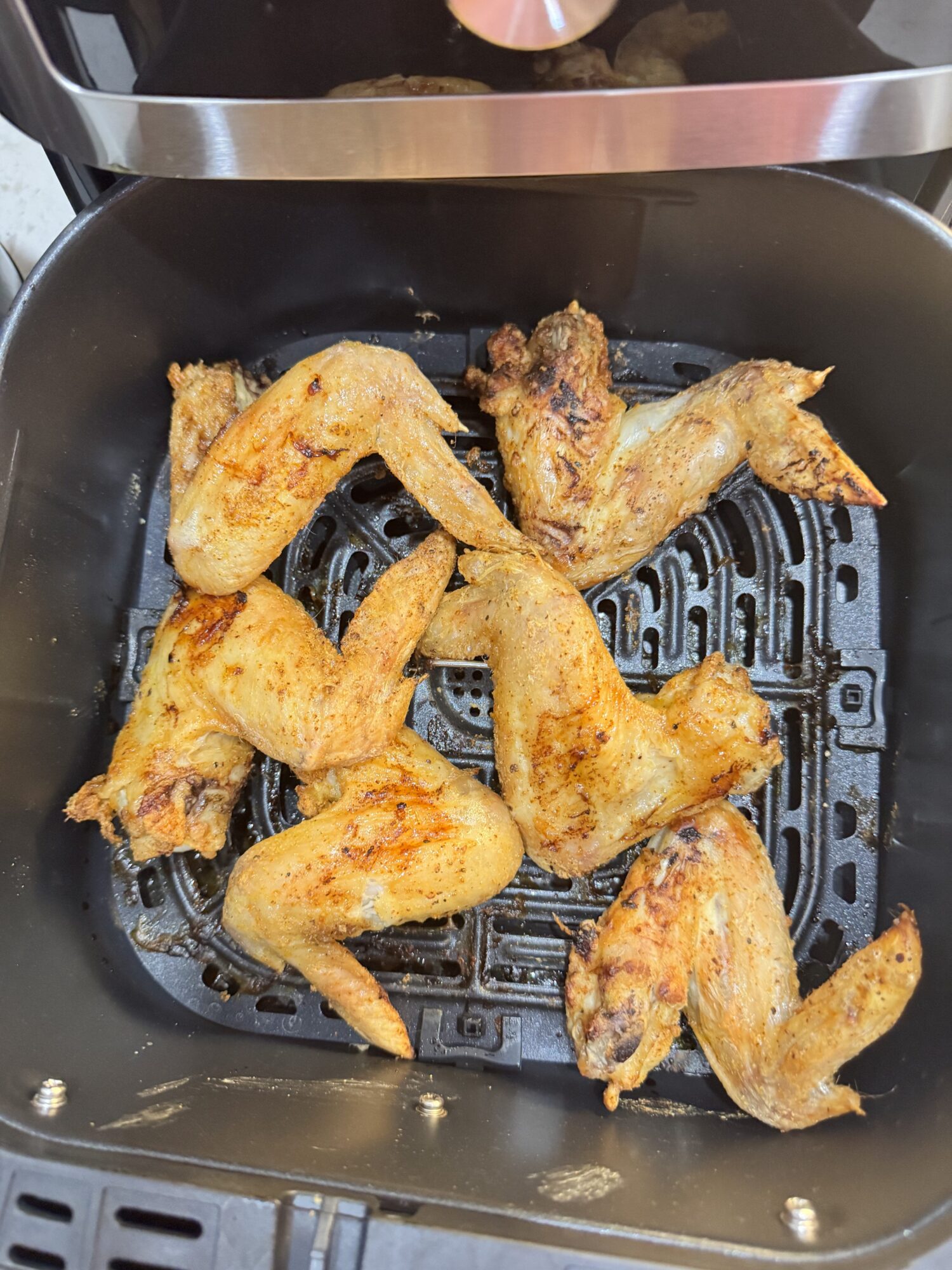 Seasoned raw chicken wings in an air fryer basket.