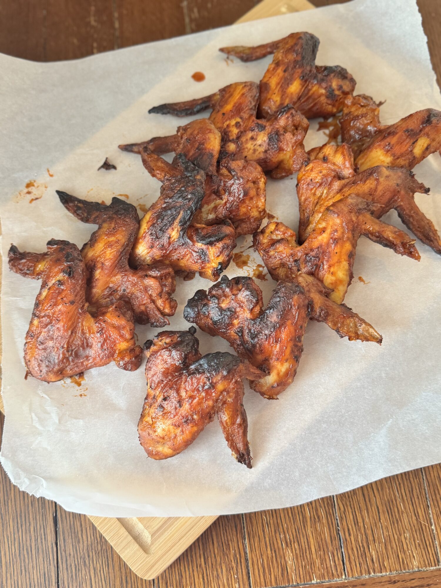 Two rows of air fryer BBQ chicken wings on a sheet of parchment paper.