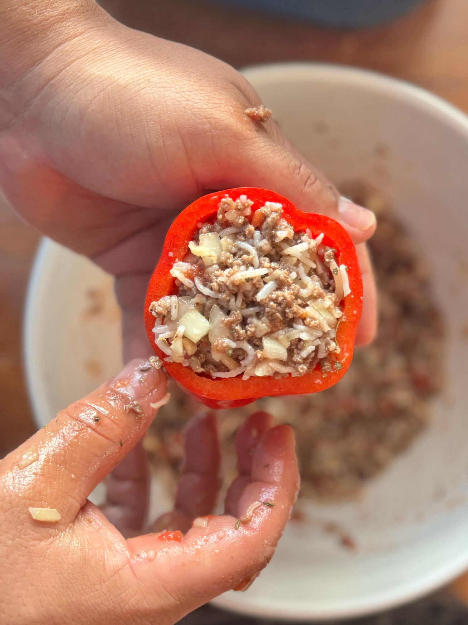 A hand holding a red bell pepper stuffed with ground beef and rice.
