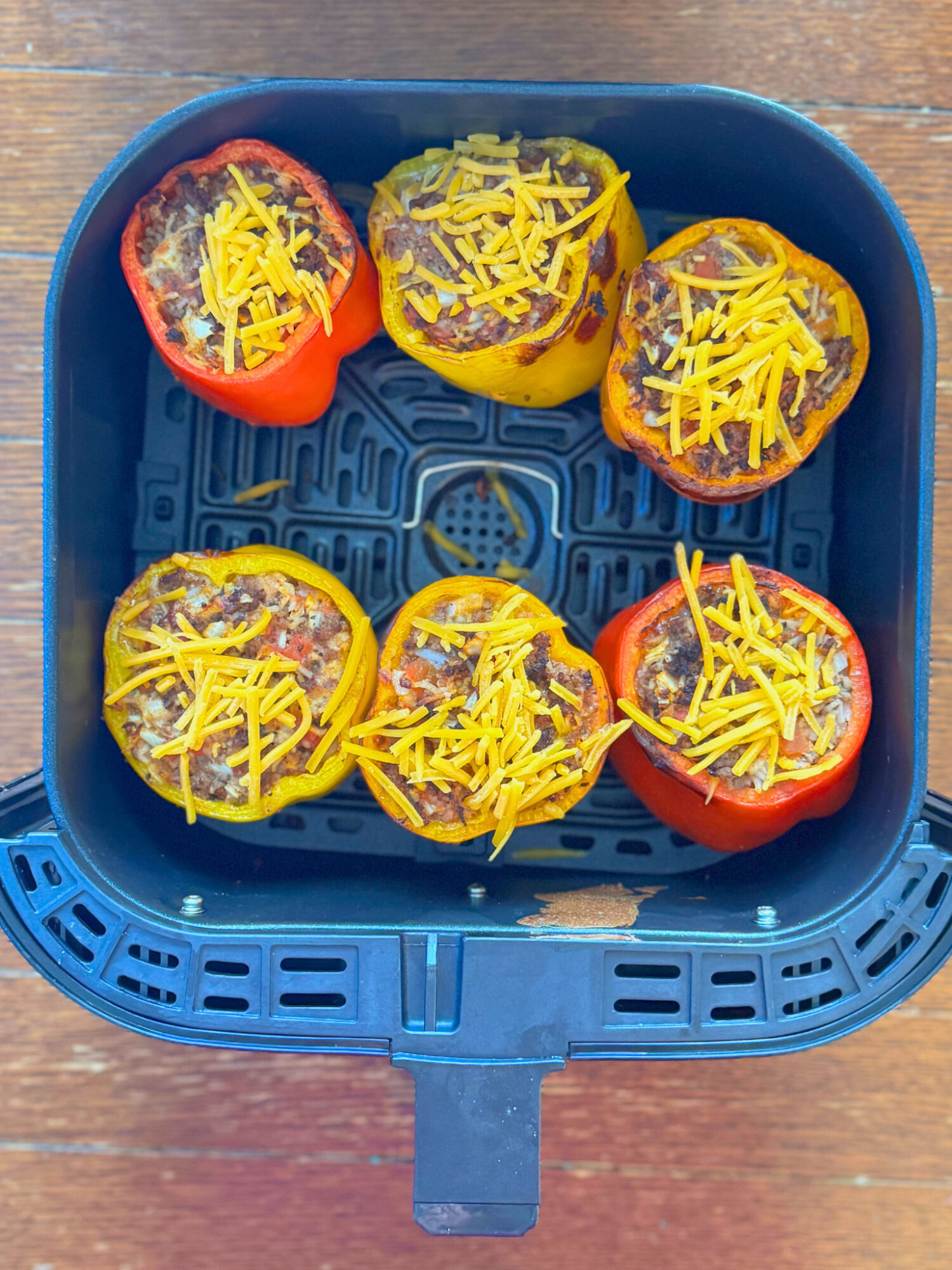 Stuffed peppers in an air fryer basket topped with cheese ready to cook.