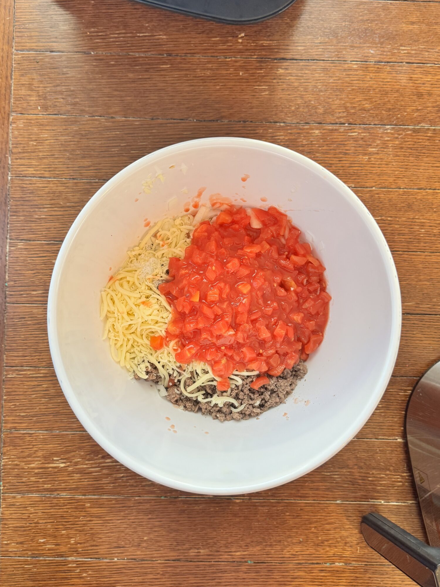 Cheese, ground beef, and diced tomato in a white bowl before getting mixed.