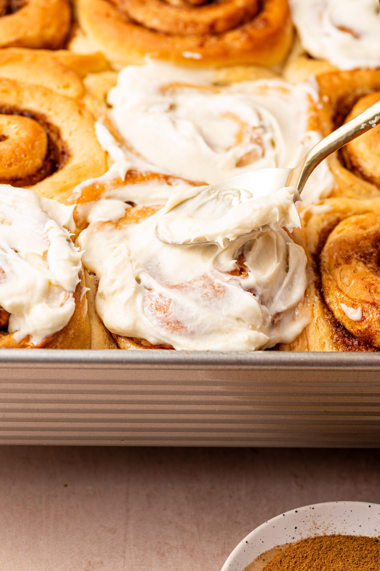 Spreading cream cheese frosting on a cinnamon roll.