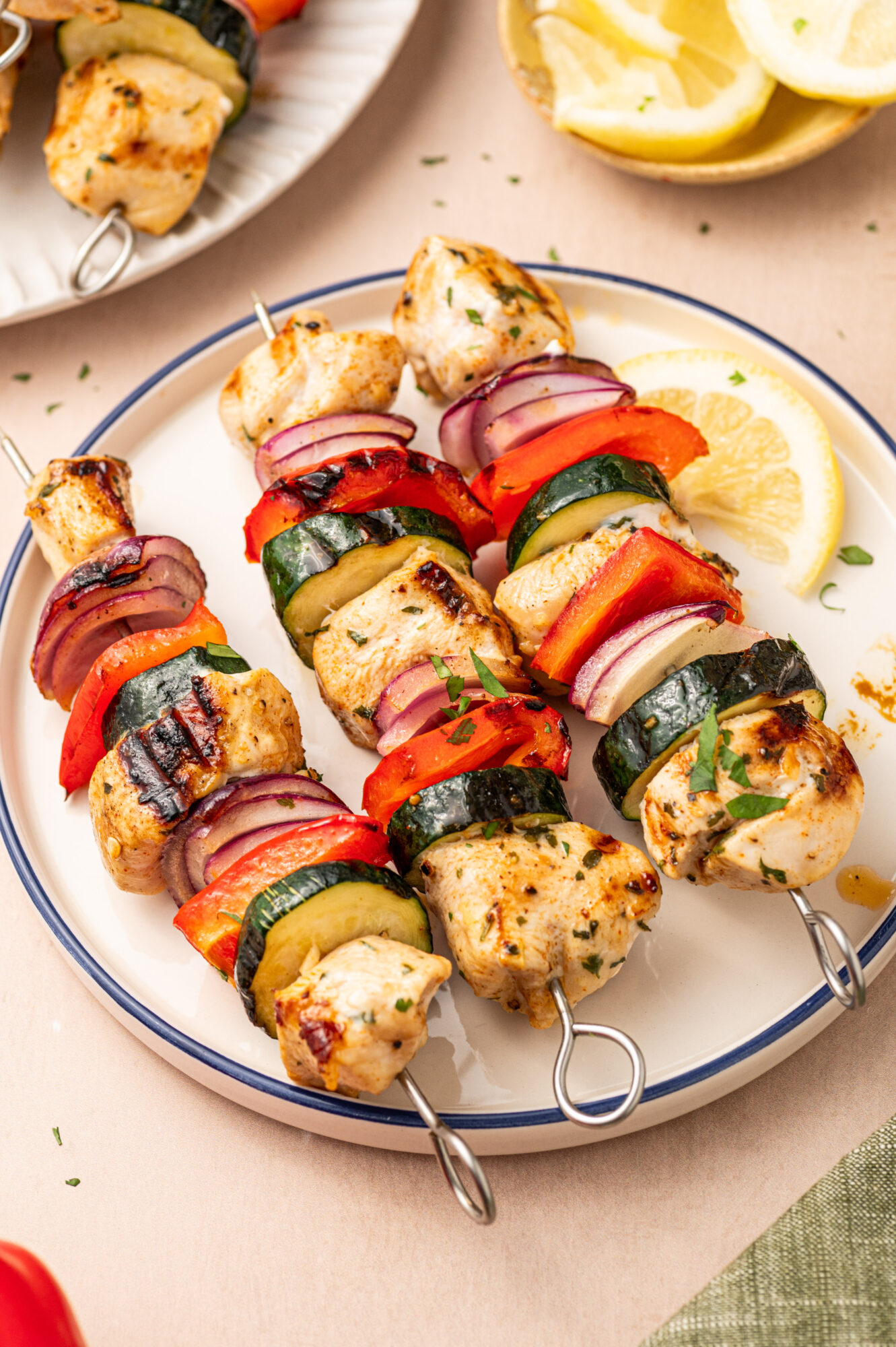 Three grilled chicken kabobs on a white plate served with a lemon wedge.