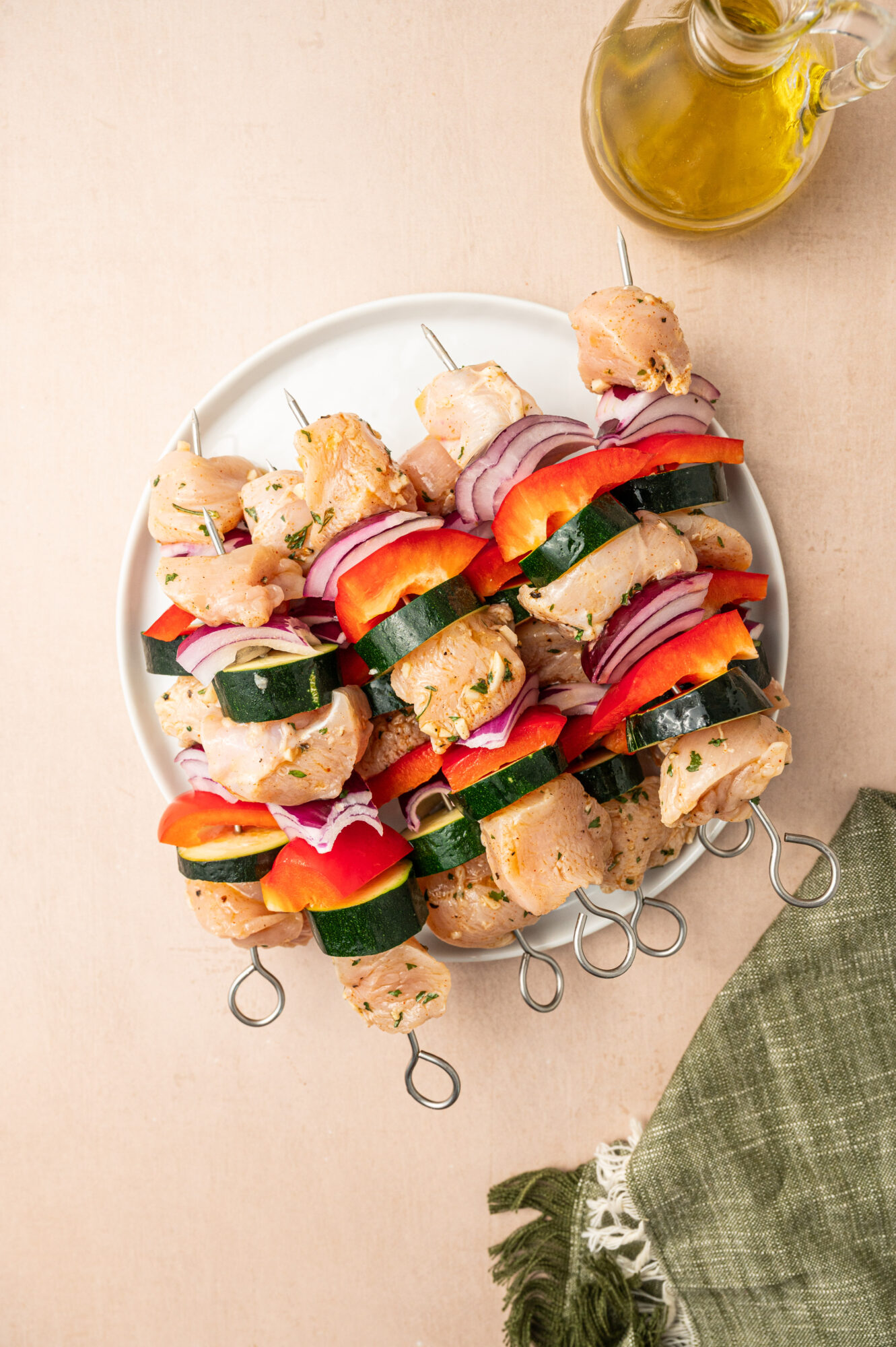 A plate of raw chicken skewers with red bell pepper, red onion, and zucchini.