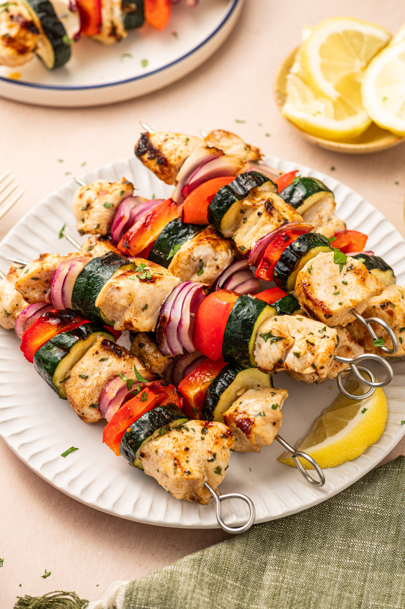 Grilled chicken kabobs on a paper plate with red onion, bell pepper, and zucchini.