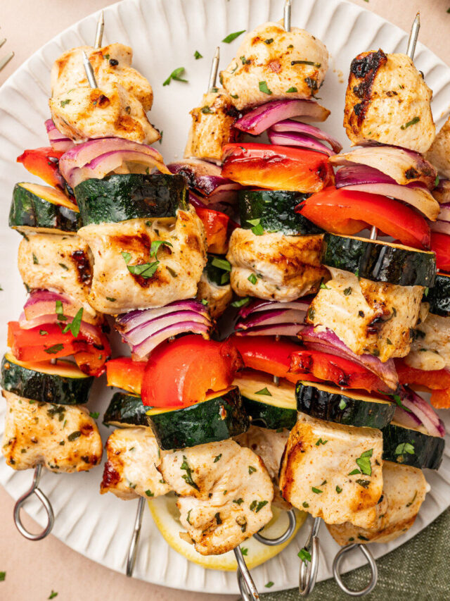 Grilled chicken kabobs on a paper plate with red onion, bell pepper, and zucchini.