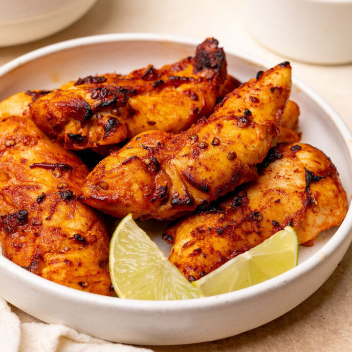 Honey chipotle chicken tenders in a white bowl with lime wedges.
