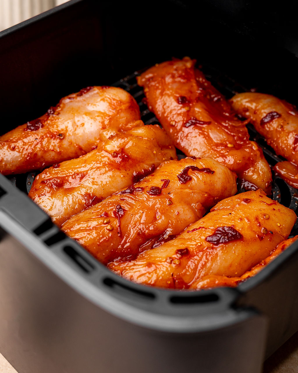Raw, seasoned chicken tenders in an air fryer basket ready to cook.