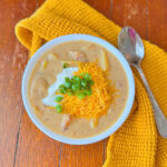 A white bowl of loaded potato soup over a rustic wooden surface.