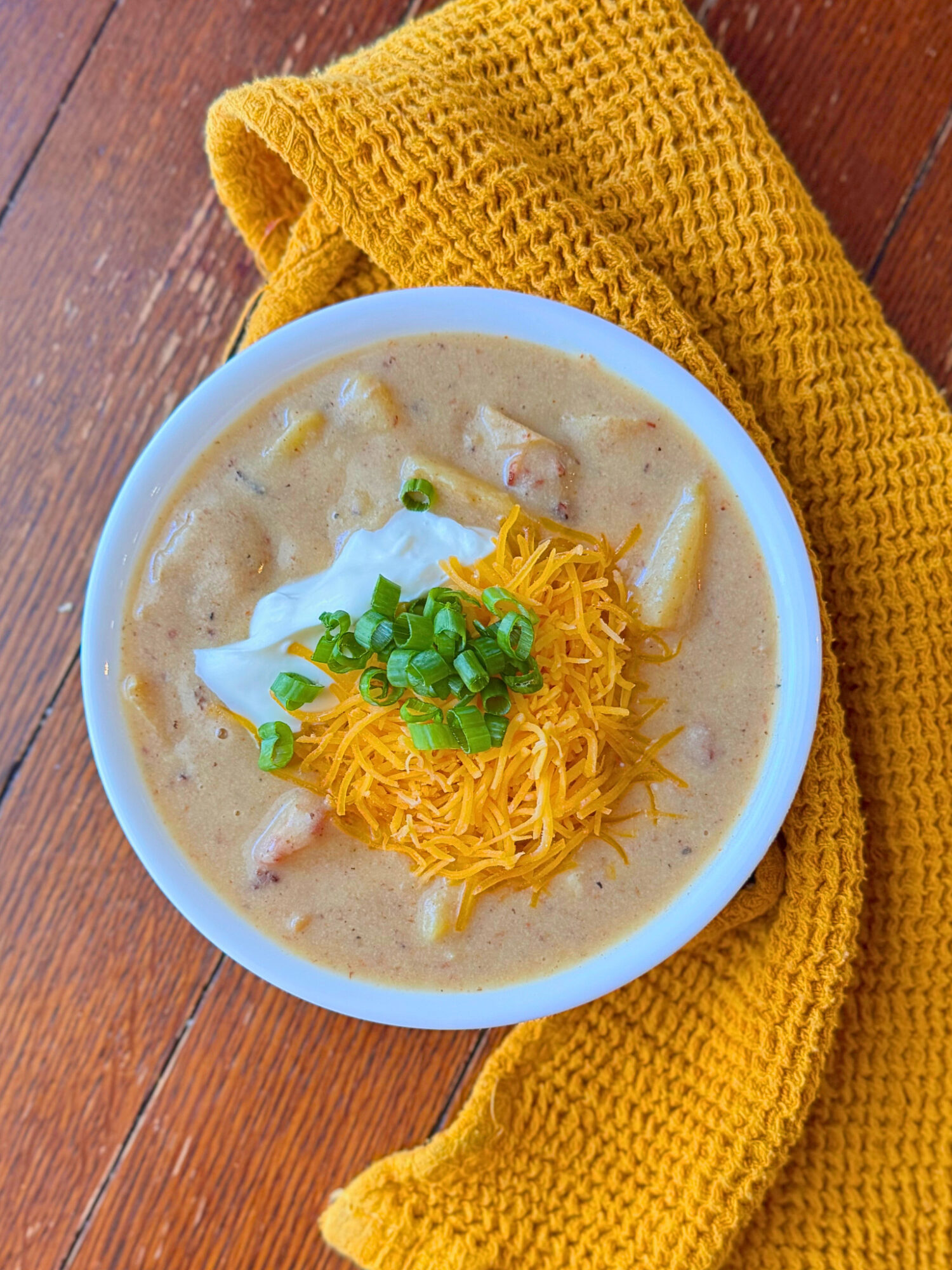 A bowl of loaed potato soup over a rustic wooden surface topped with chives, sour cream, and cheese.