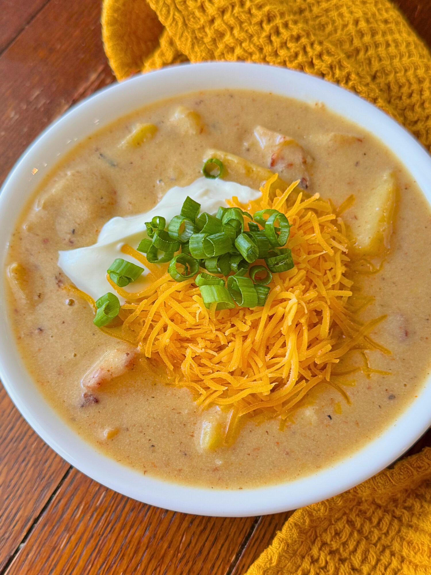 Close-up of loaded potato soup over a rustic wooden surface topped with chives, sour cream, and cheese.