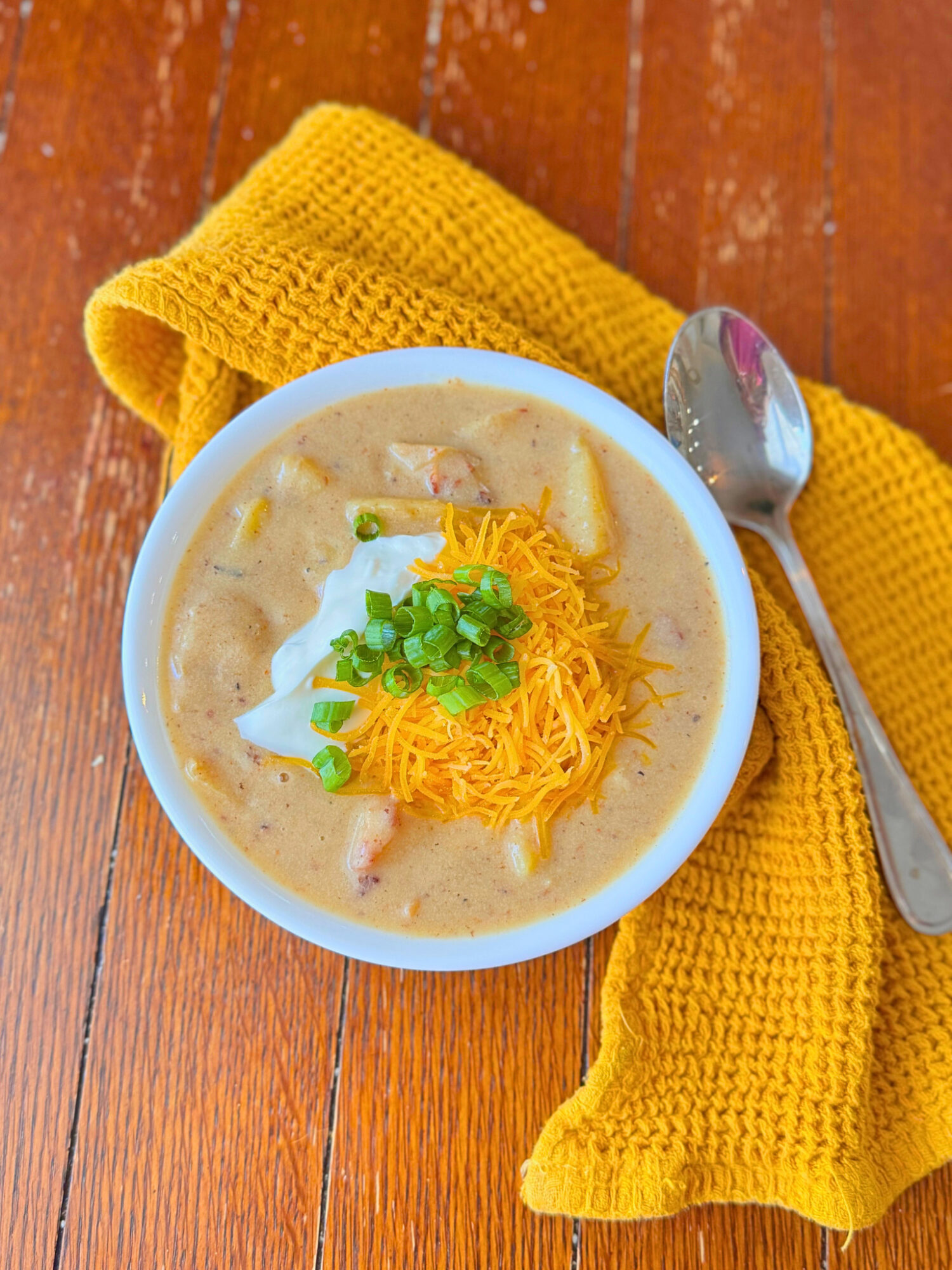 A white bowl of loaded potato soup over a rustic wooden surface.