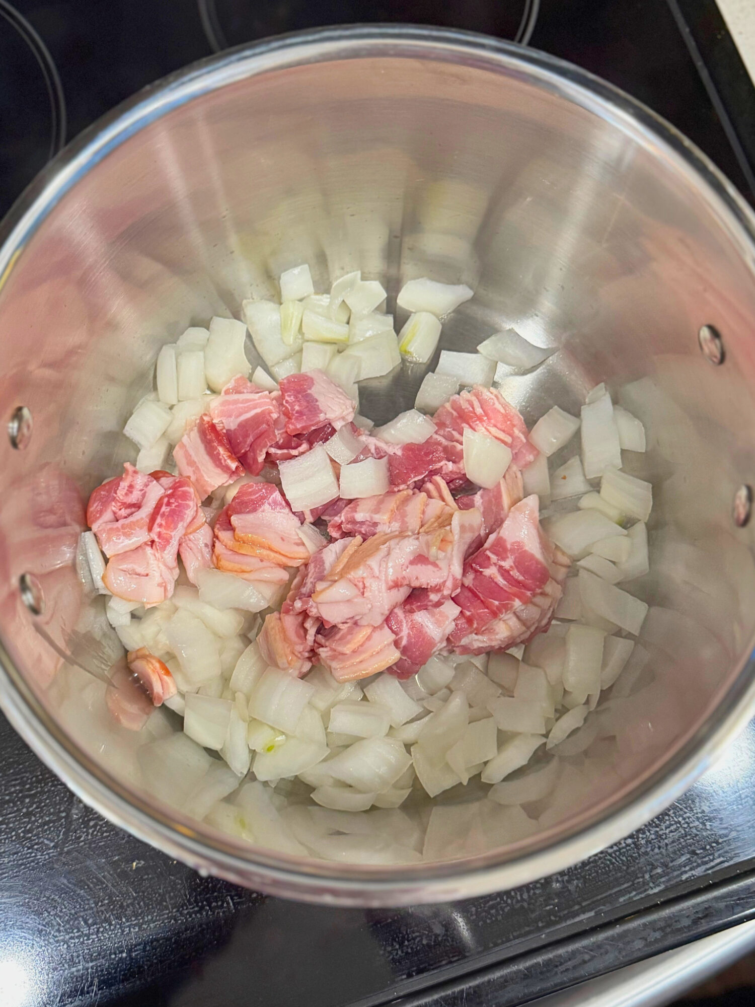 Raw bacon and onions in a large pot over the stove.