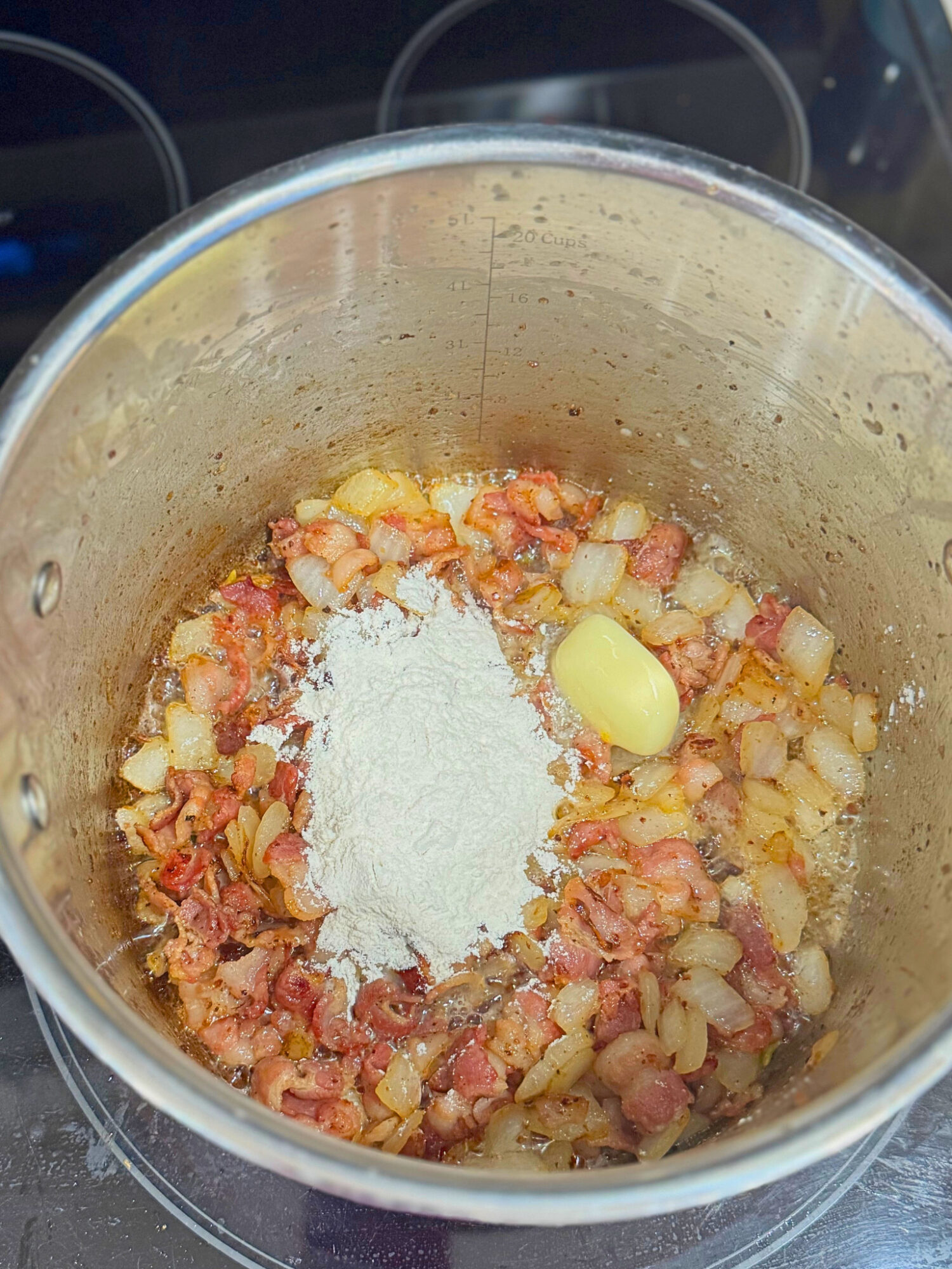 Adding flour to a large pot of cooked bacon and onions.