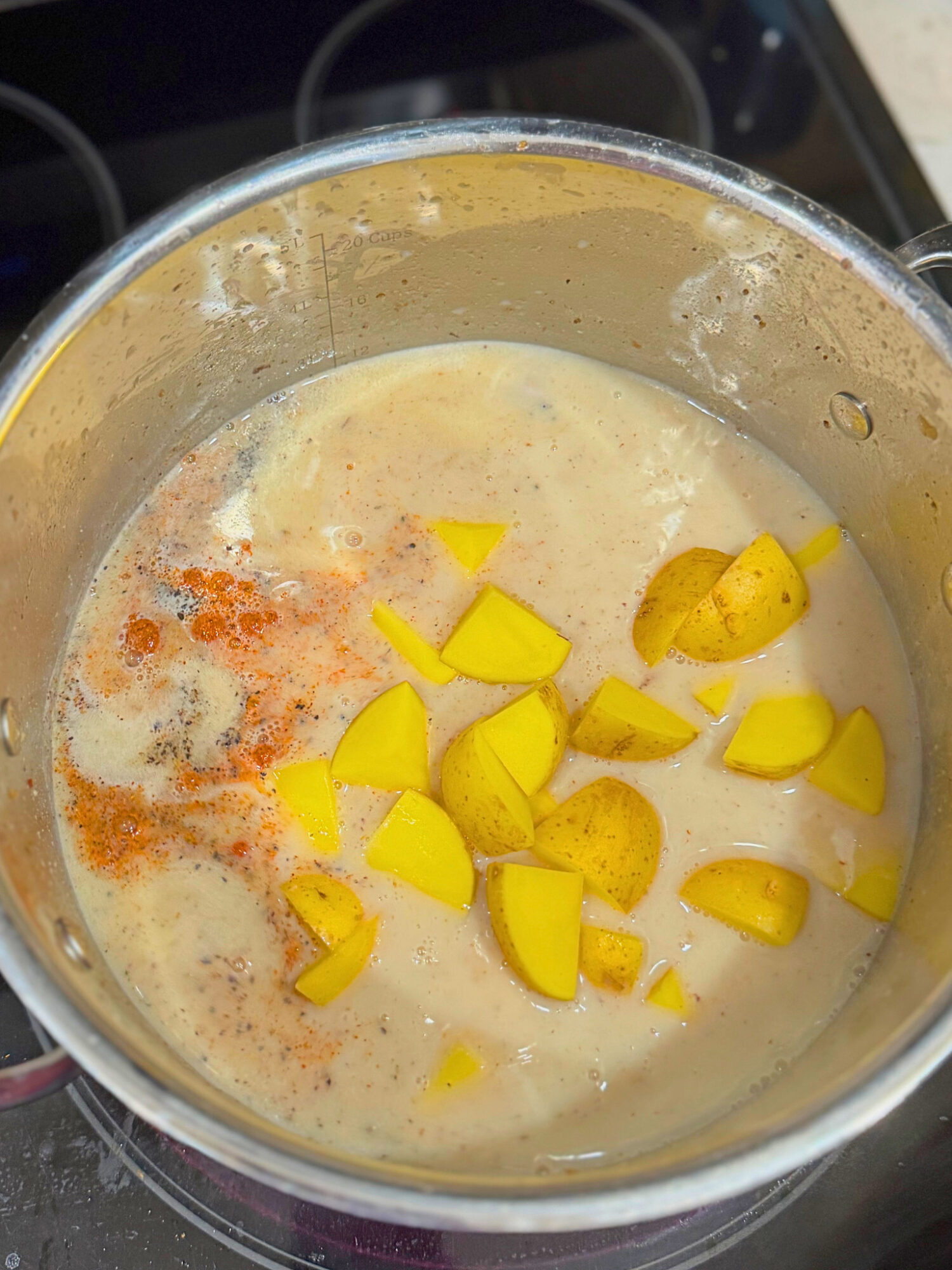 Potatoes, spices, milk, and broth mixing together in a large pot.