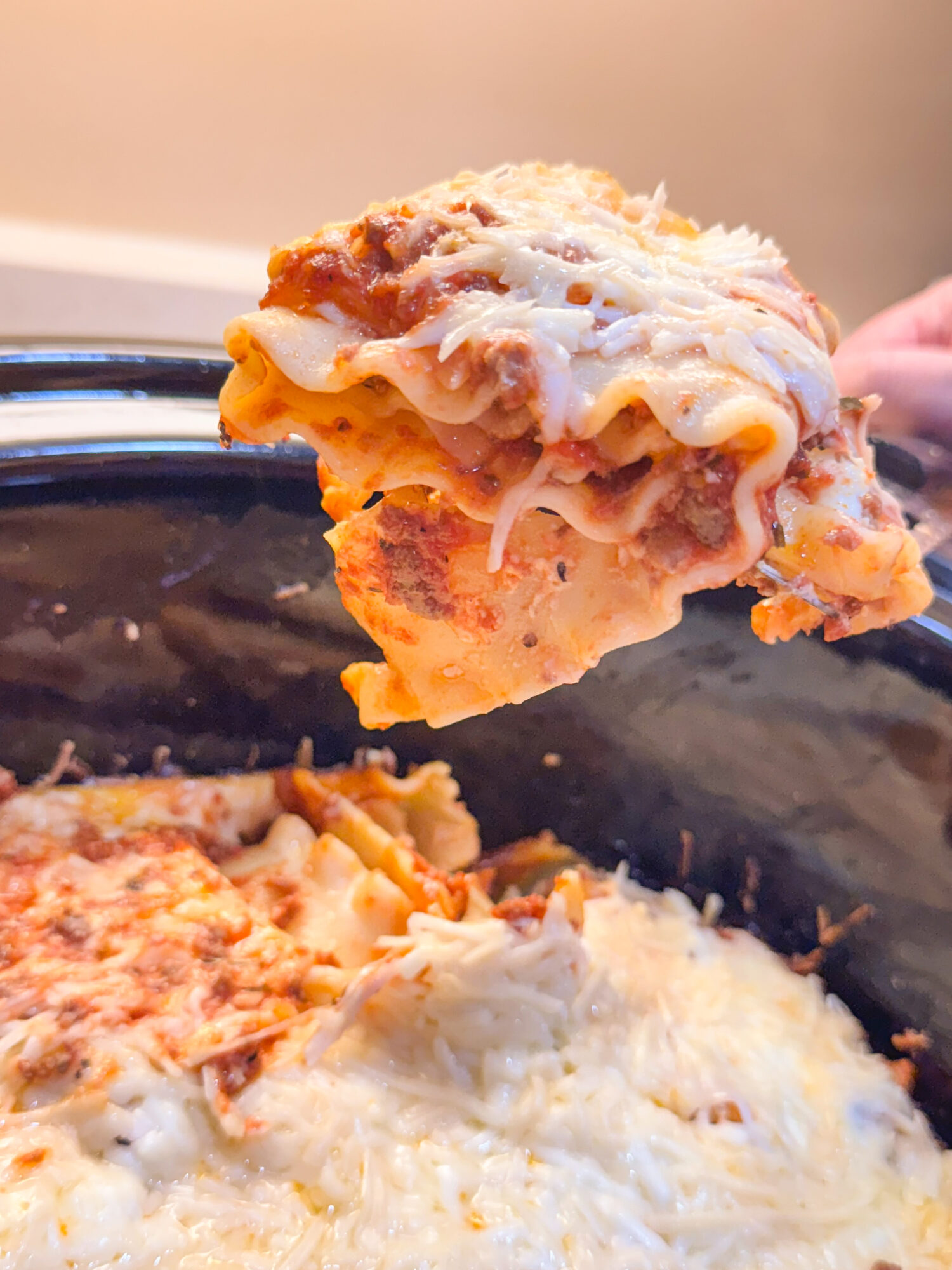 Lifting a piece of lasagna out of the slow cooker with a spatula.