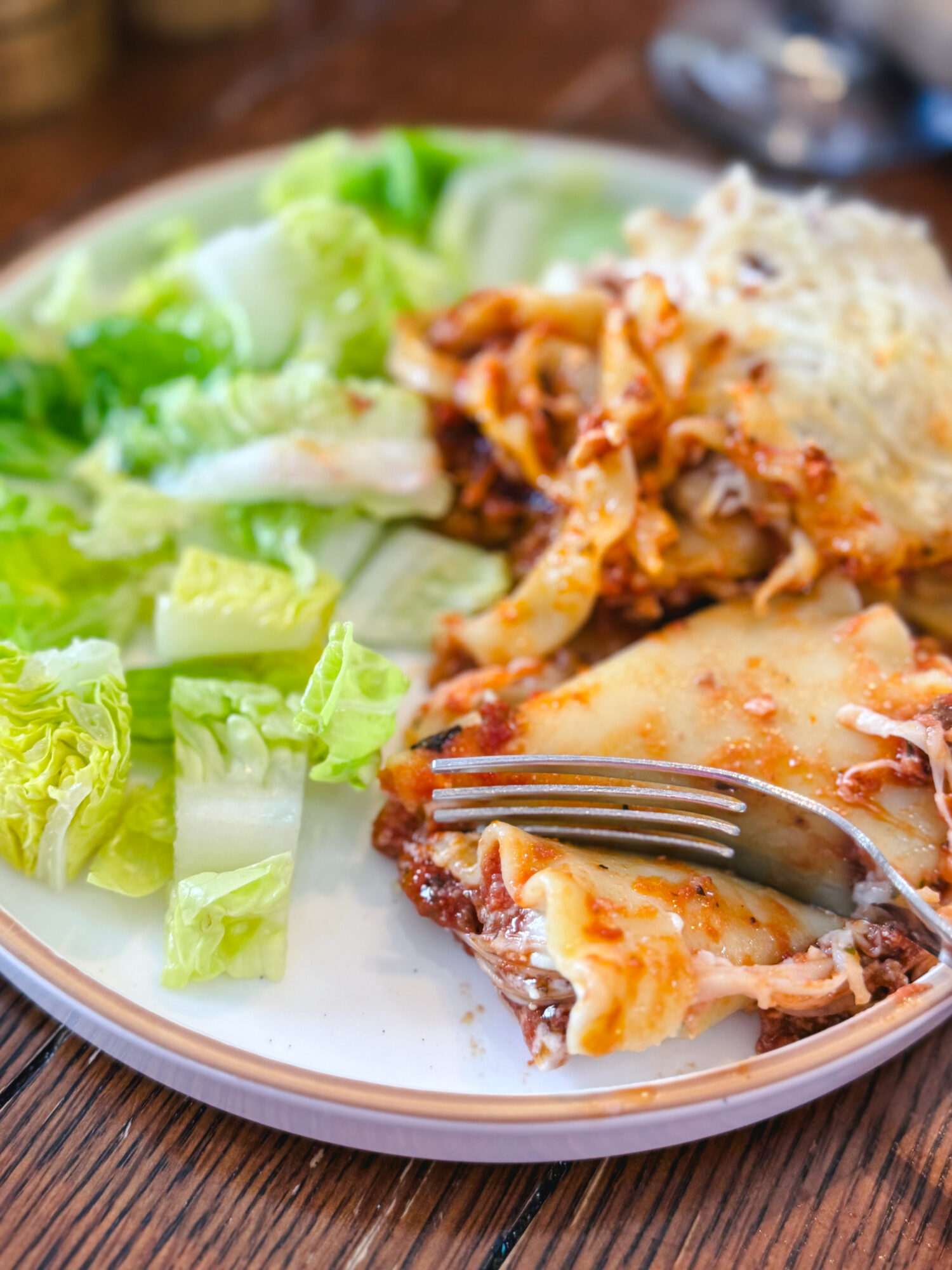 A fork digging into a plate of lasagna with a side salad.