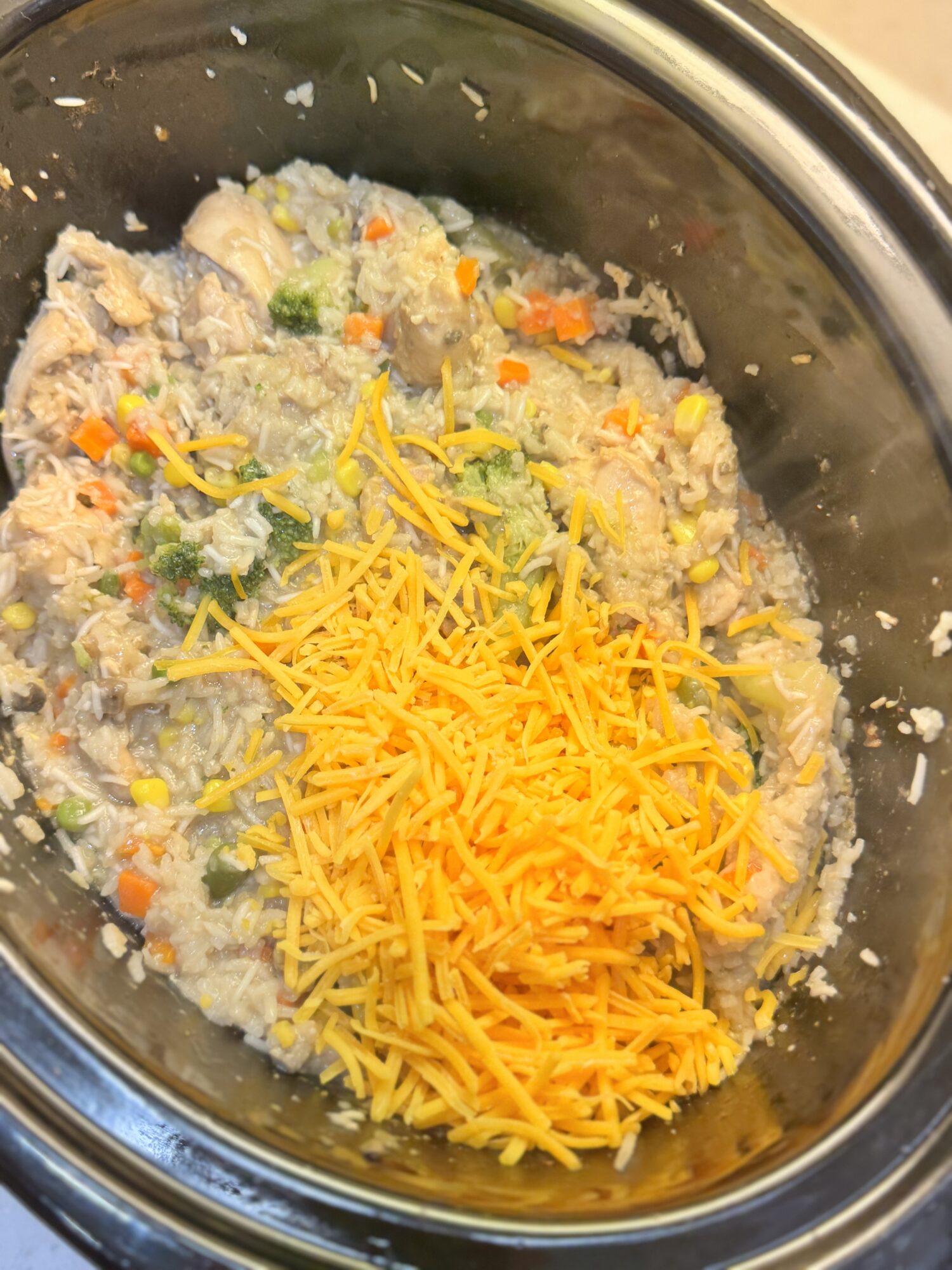 Adding shredded cheddar cheese to a slow cooker of chicken and rice.