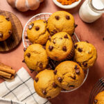 A basket of chocolate chip and pumpkin muffins surrounded by ingredients.