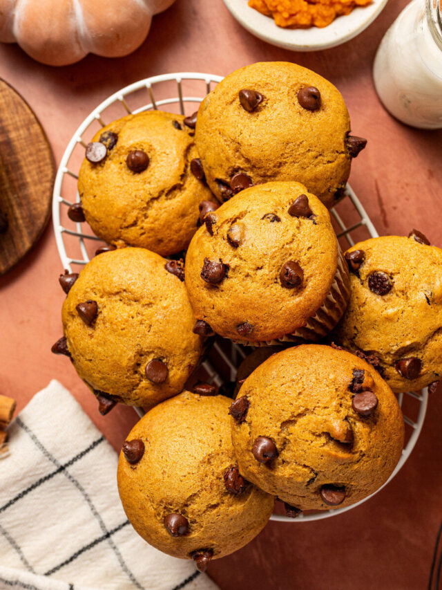A basket of chocolate chip and pumpkin muffins surrounded by ingredients.
