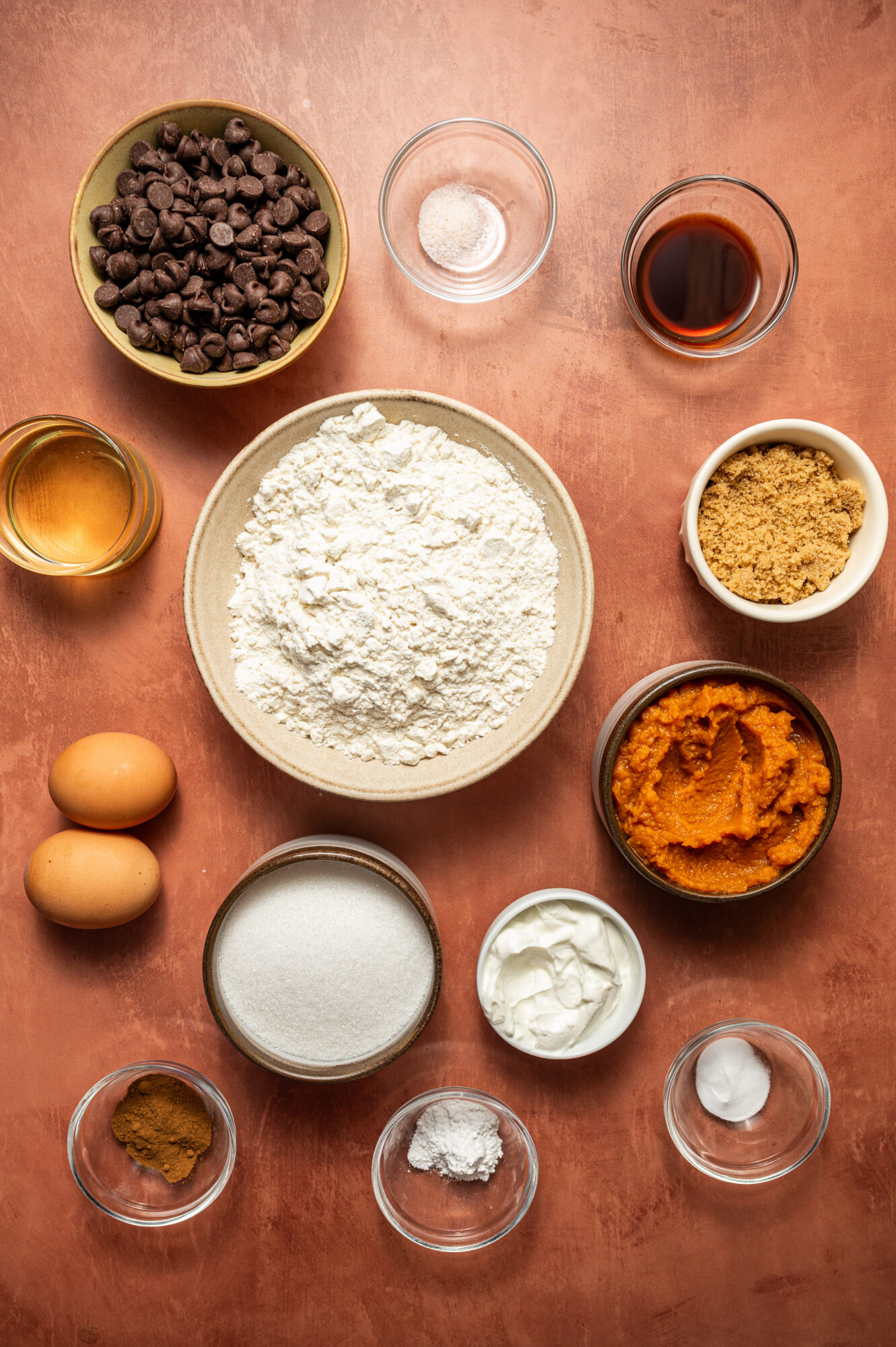 Ingredients for chocolate chip and pumpkin muffins on a rose colored surface.
