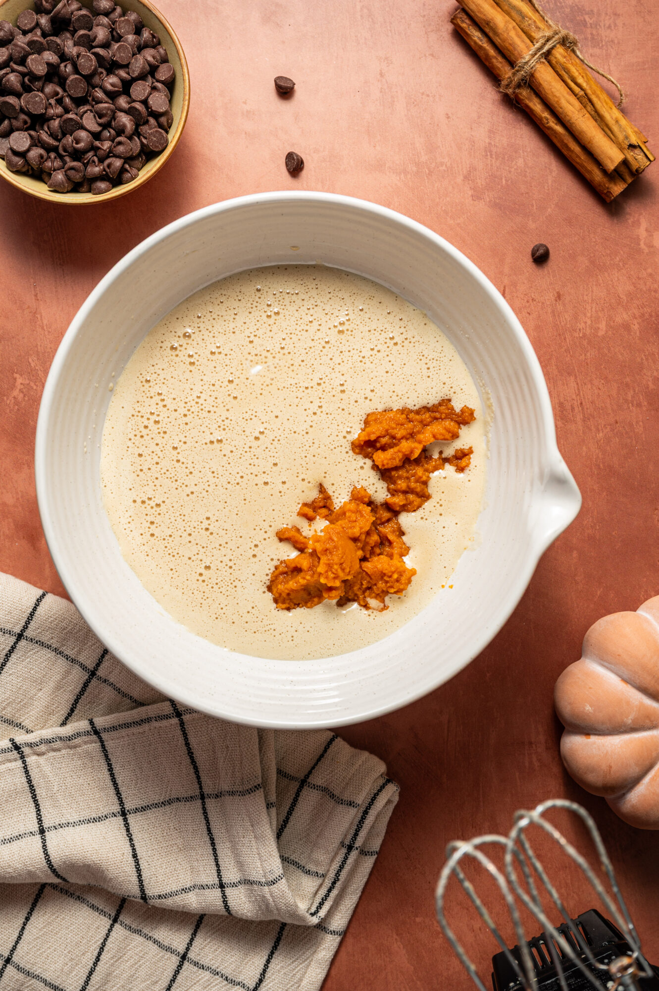 Adding pumpkin puree to a bowl of wet ingredients.